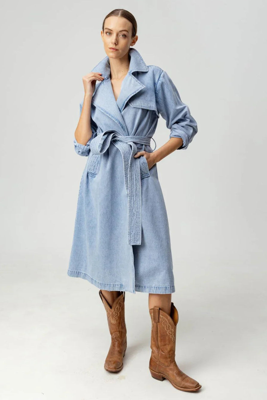 Woman wearing a light blue trench coat and brown boots on a white background